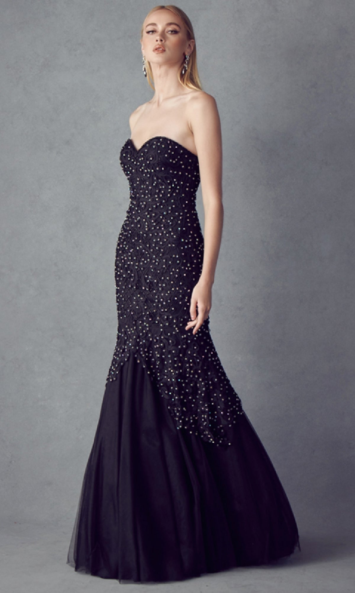 A woman models the Long Mermaid Prom Dress: Juliet 644, a strapless, floor-length black gown adorned with small pearls, standing against a plain gray background.